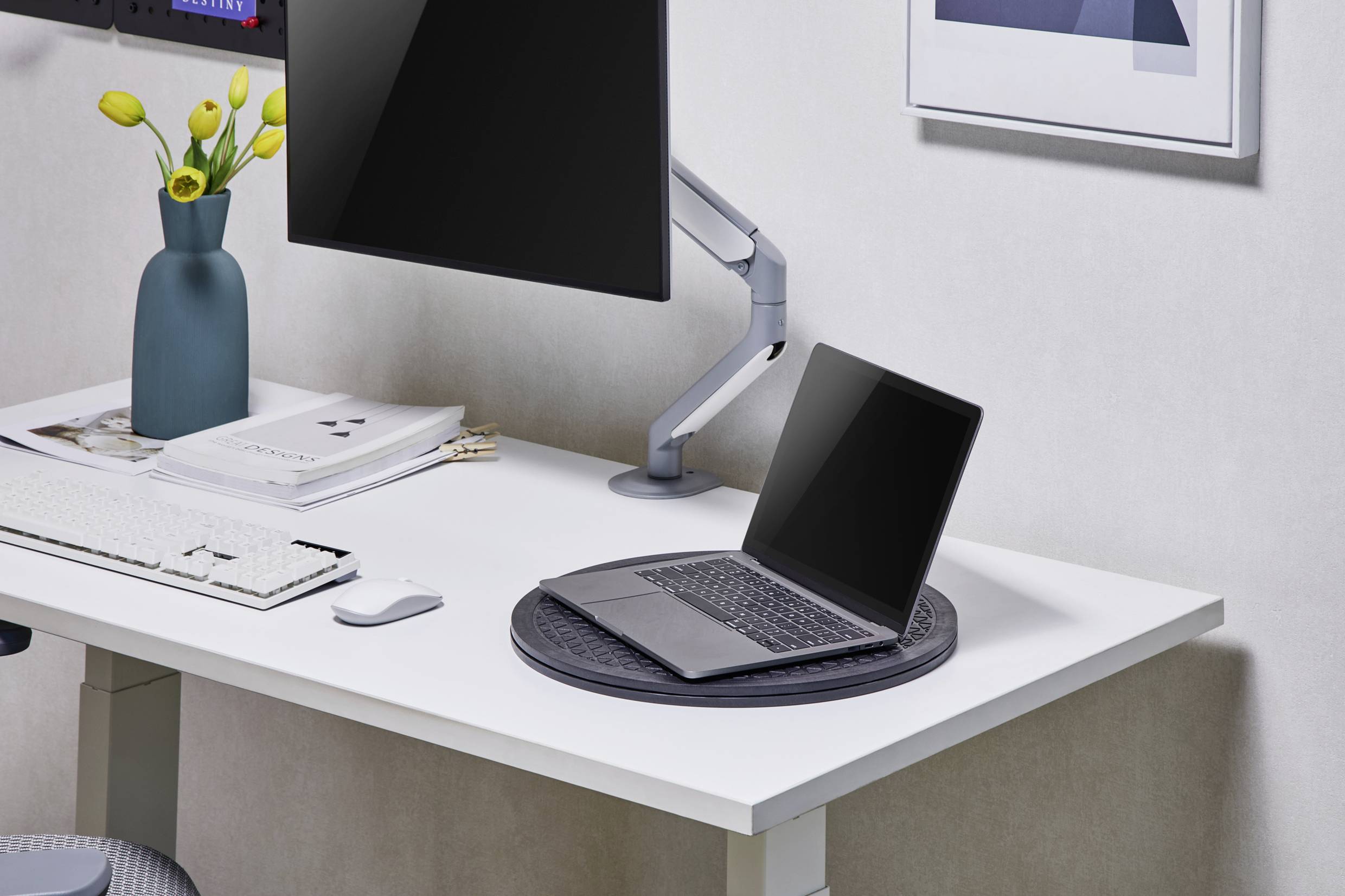 A modern desk with a laptop, a monitor, a keyboard and a vase of yellow tulips.