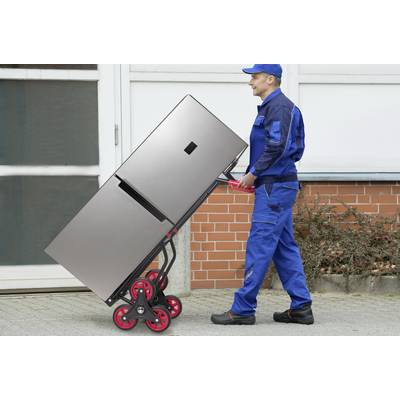 A man in a blue uniform is transporting a large fridge using a specialised trolley in front of a building.