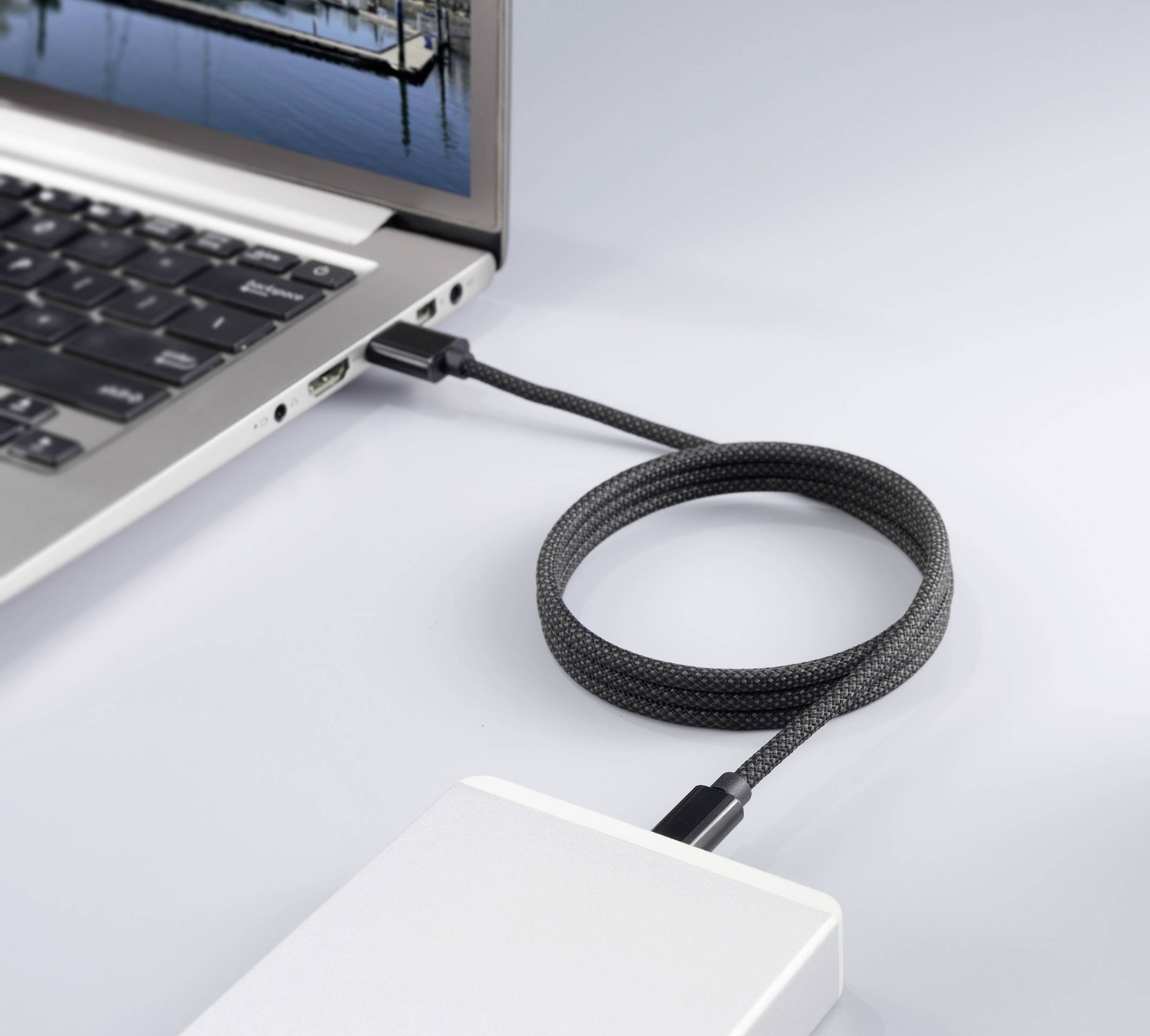 An external storage device is connected to a laptop via a cable. The laptop screen displays an image of a harbour.