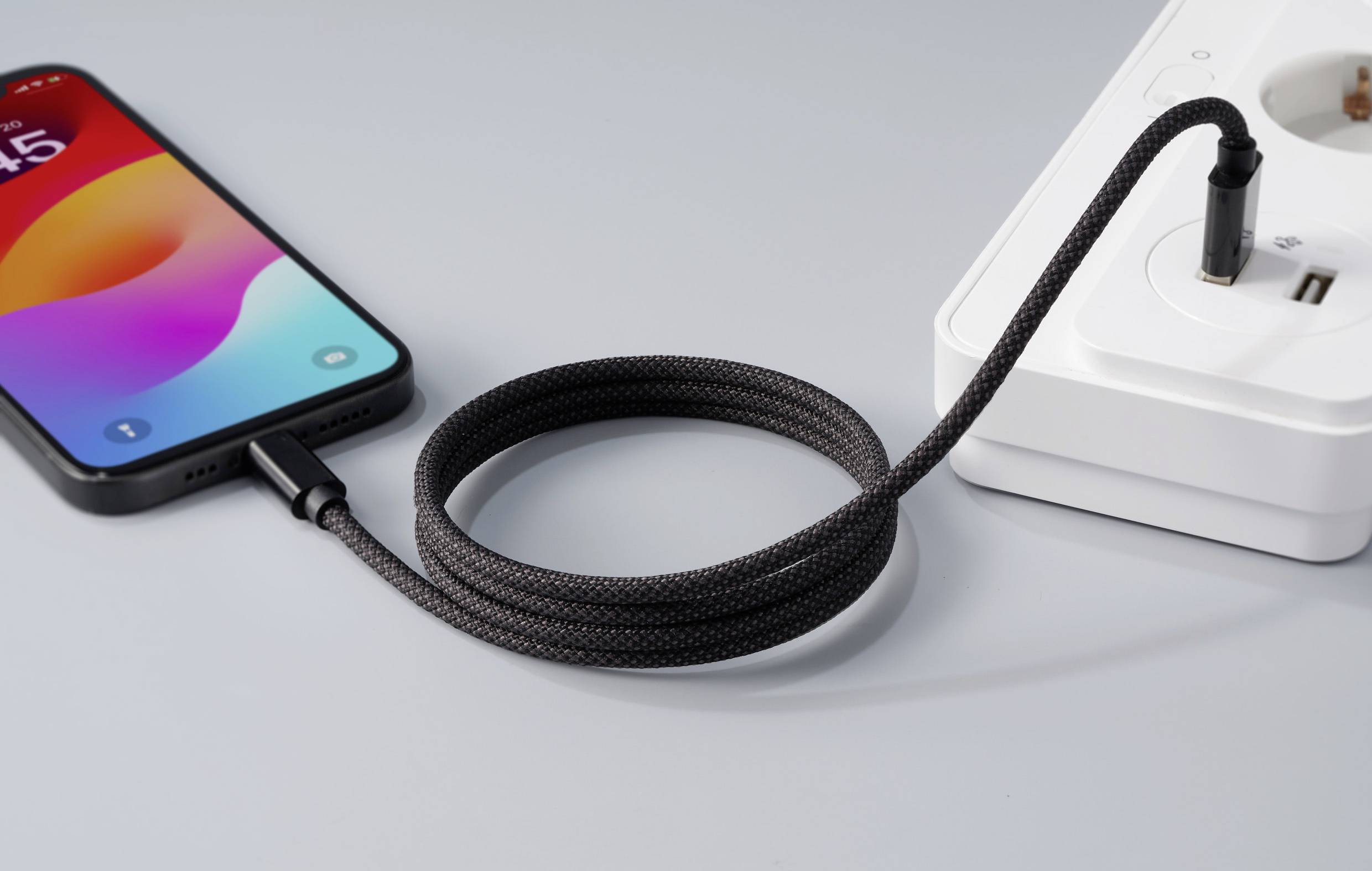 A smartphone is being charged with a braided charging cable on a white power strip.