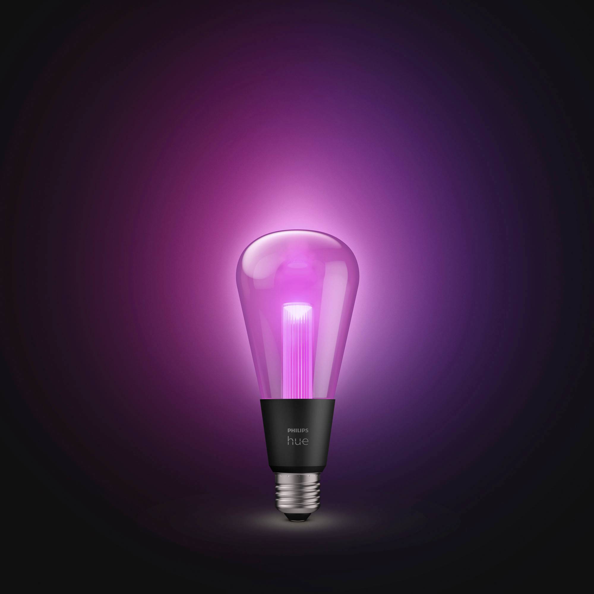 A LED light bulb glows with violet light. It stands against a dark background and creates a soft, colourful aura.