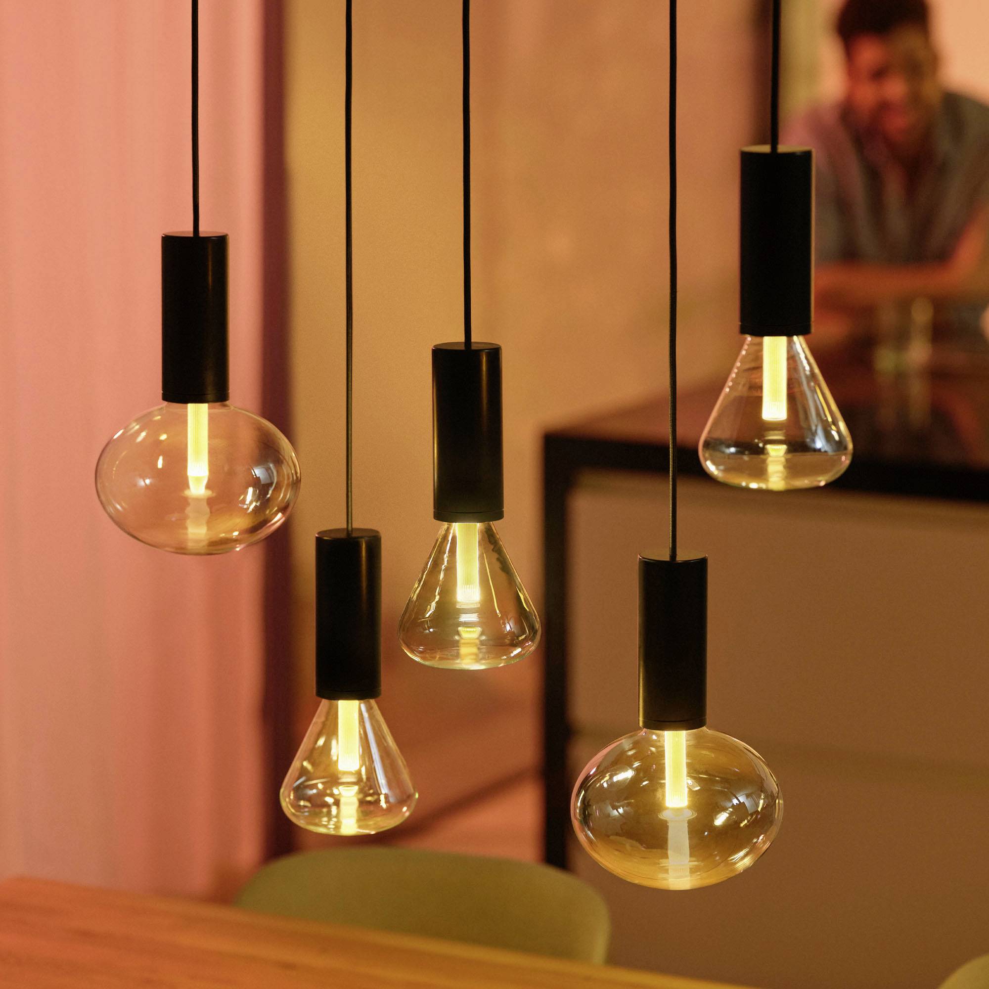 Modern pendant lights glow warmly over a table. The surroundings have a cosy atmosphere with a soft orange light.