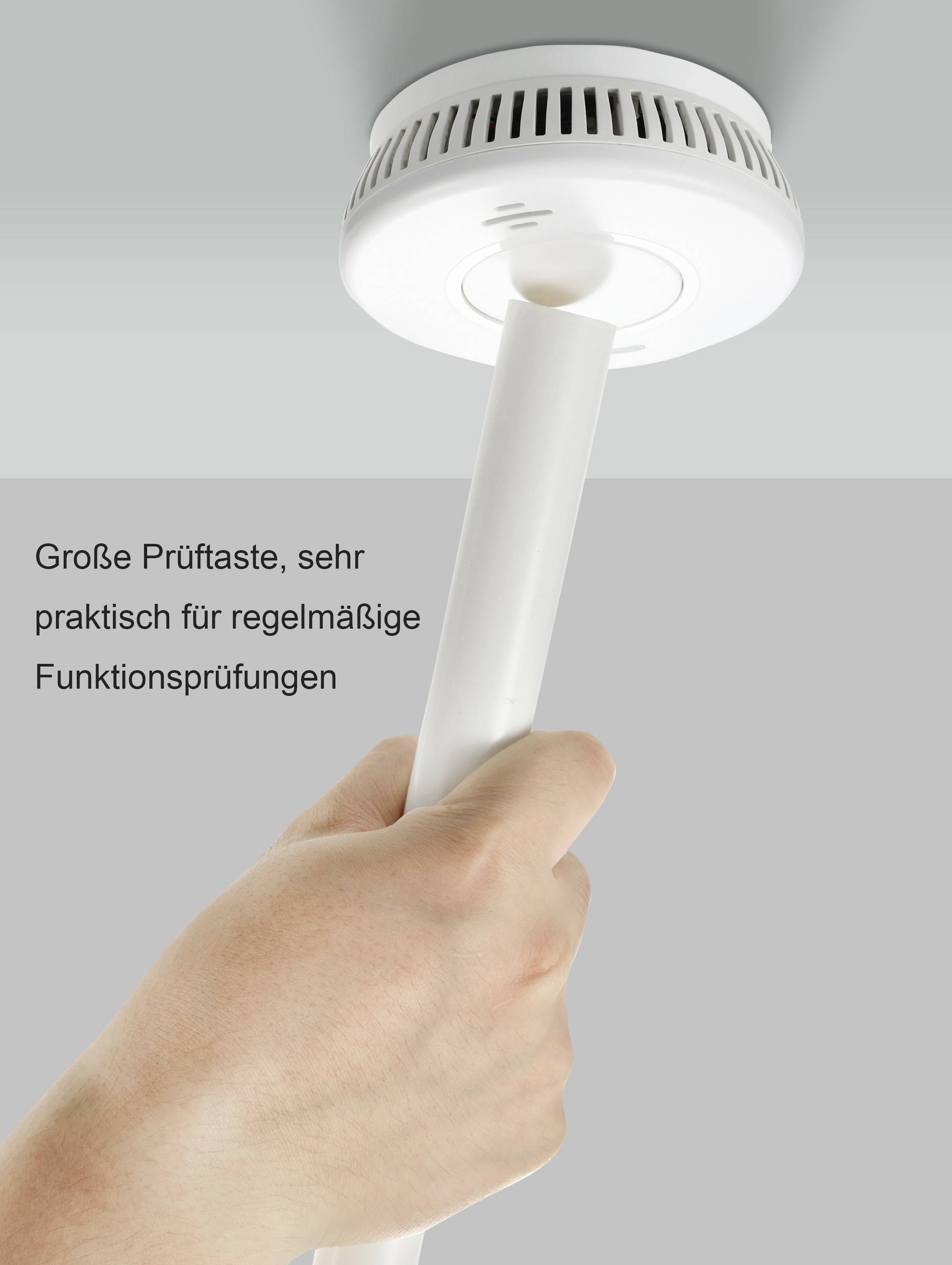A hand presses a long rod against the large test button of a smoke detector to regularly check its functionality.
