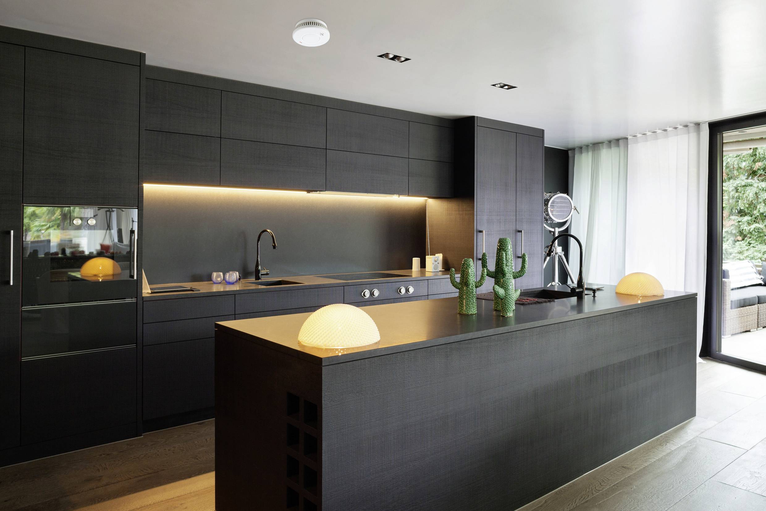 Modern kitchen with dark cabinets, illuminated worktop and large kitchen island. Large windows overlooking a garden.