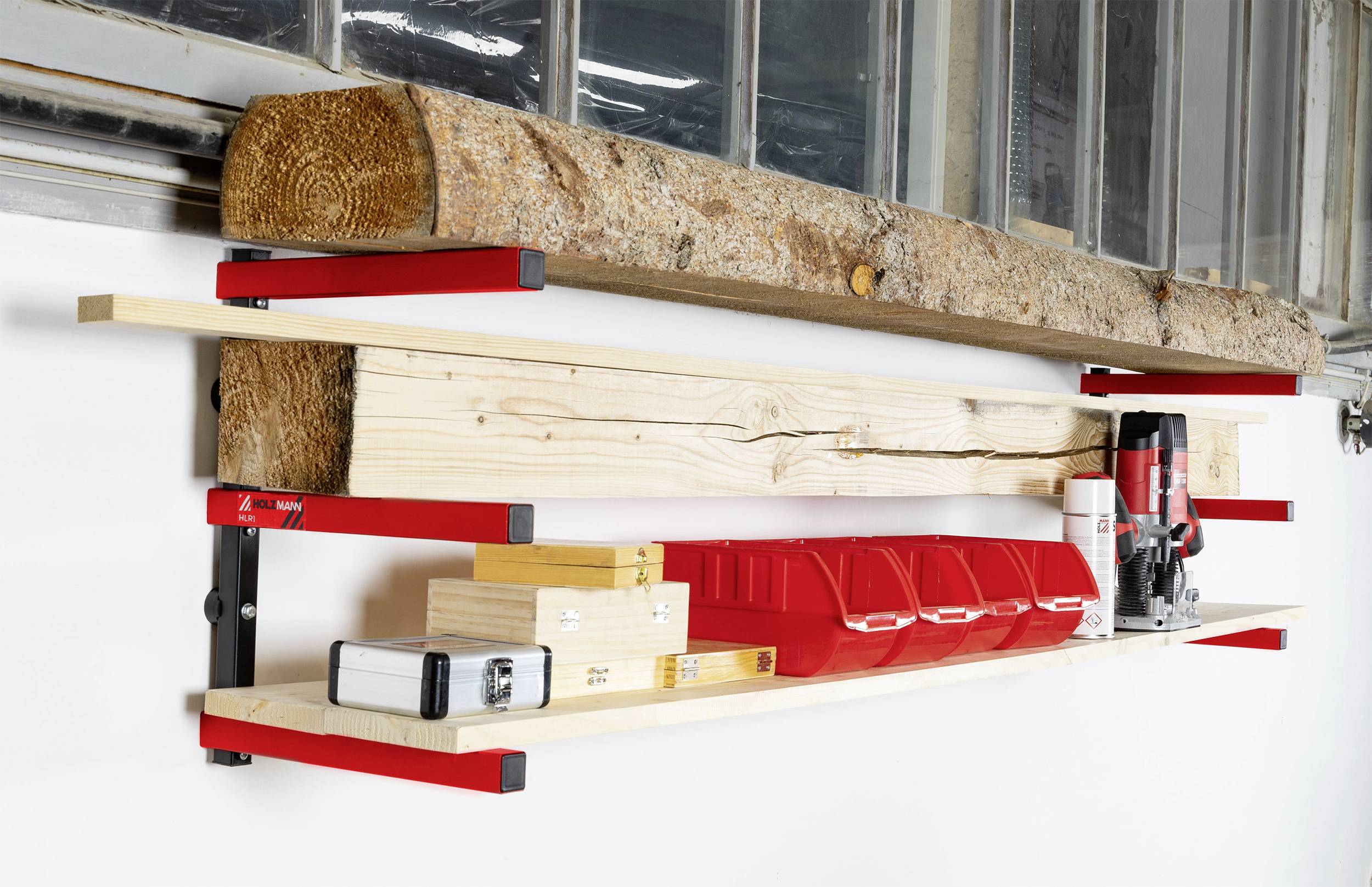 A three-tier wall-mounted shelving unit with a red frame holds wooden pieces, a spirit level, tools and containers for screws in a workshop.