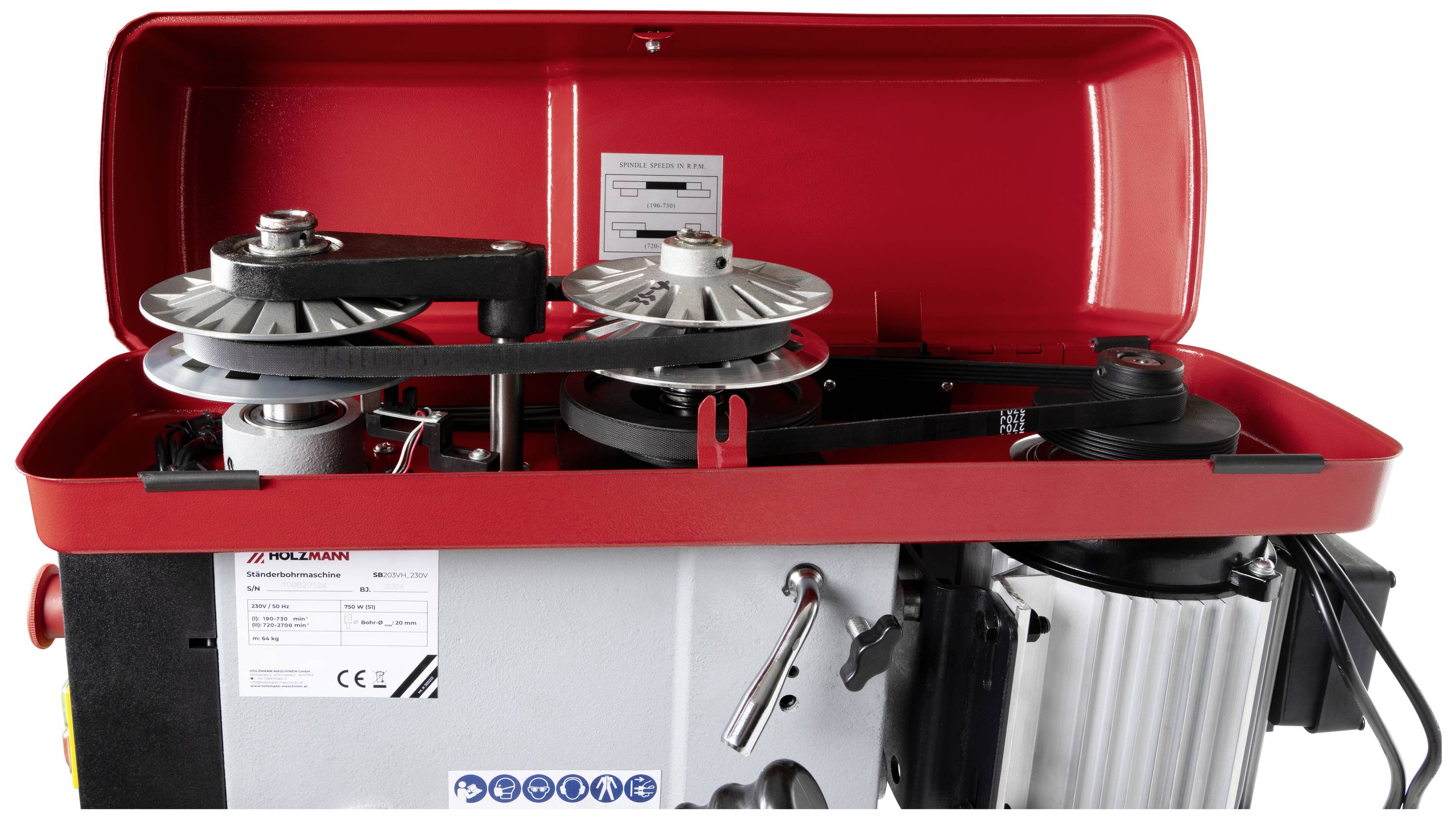 An opened red metal box reveals the interior of a machine with belts and rollers. Signs and control elements are visible.