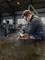 A man is working in a workshop and grinding metal with an angle grinder, sparks flying. He is wearing safety glasses and ear protection.