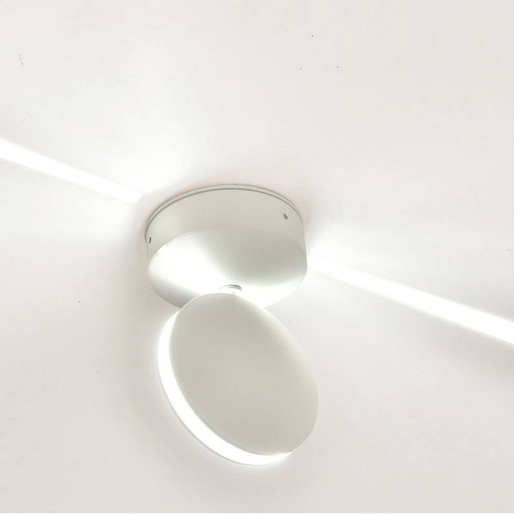 A round, modern ceiling spotlight made of metal illuminates a room. The light is bright and evenly distributed, emphasising the minimalist design.