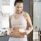 A woman is holding an electrical device against her stomach in a bright room. She appears to be using it for some kind of skincare treatment.