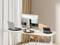 A desk with a laptop, a large monitor and a keyboard. A wooden chair stands beside it. The room is brightly lit.