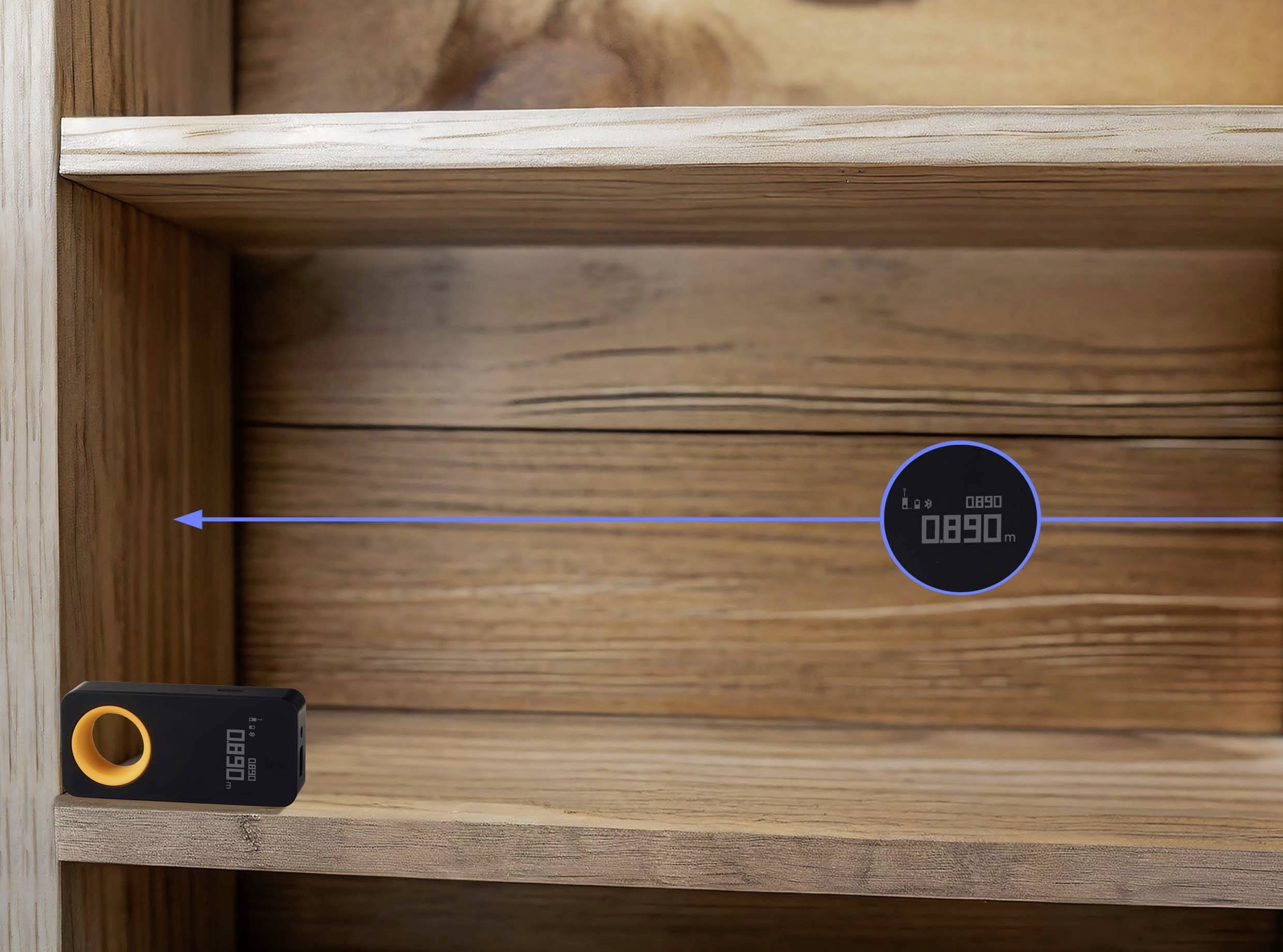 Laser distance meter measures the distance between a black device with an orange button and a wooden floor shelf. Display reading: '089.0'.