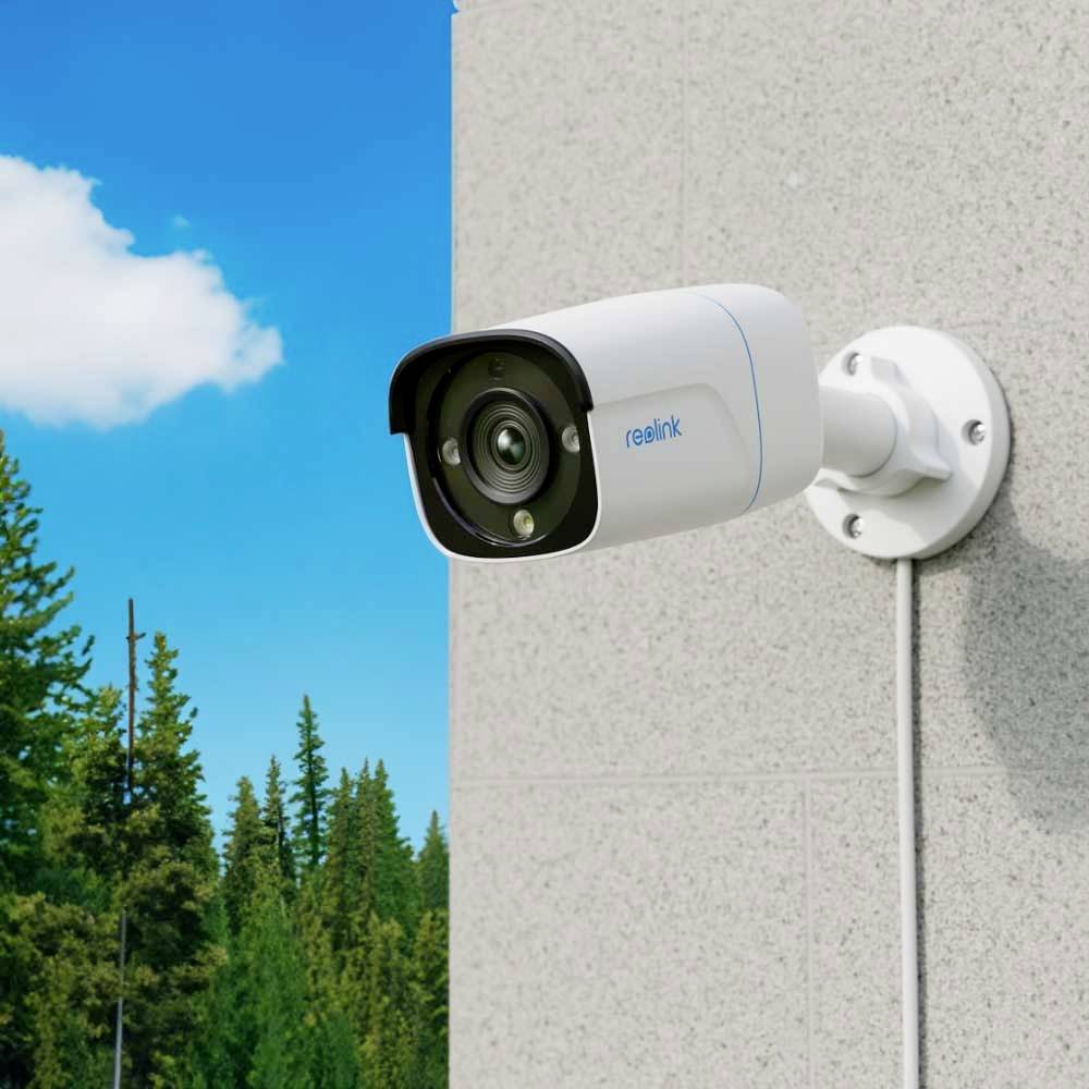 Security camera mounted on a wall, looking out over a forest under a clear sky.