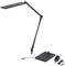 A modern, black desk lamp with an adjustable arm and rectangular lamp head. The matching power adapter lies beside it.