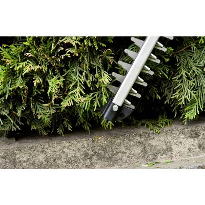 Hedge trimmer cutting a green hedge; close-up, focus on sharp blades and dense branches.
