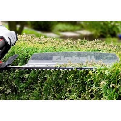 A gardener is trimming a hedge with an electric hedge trimmer. The trimmer bears the brand name, and the background shows green foliage.