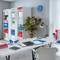 A modern office, organised with shelves full of folders in red, blue and white. A desk with a lamp, plants and accessories.