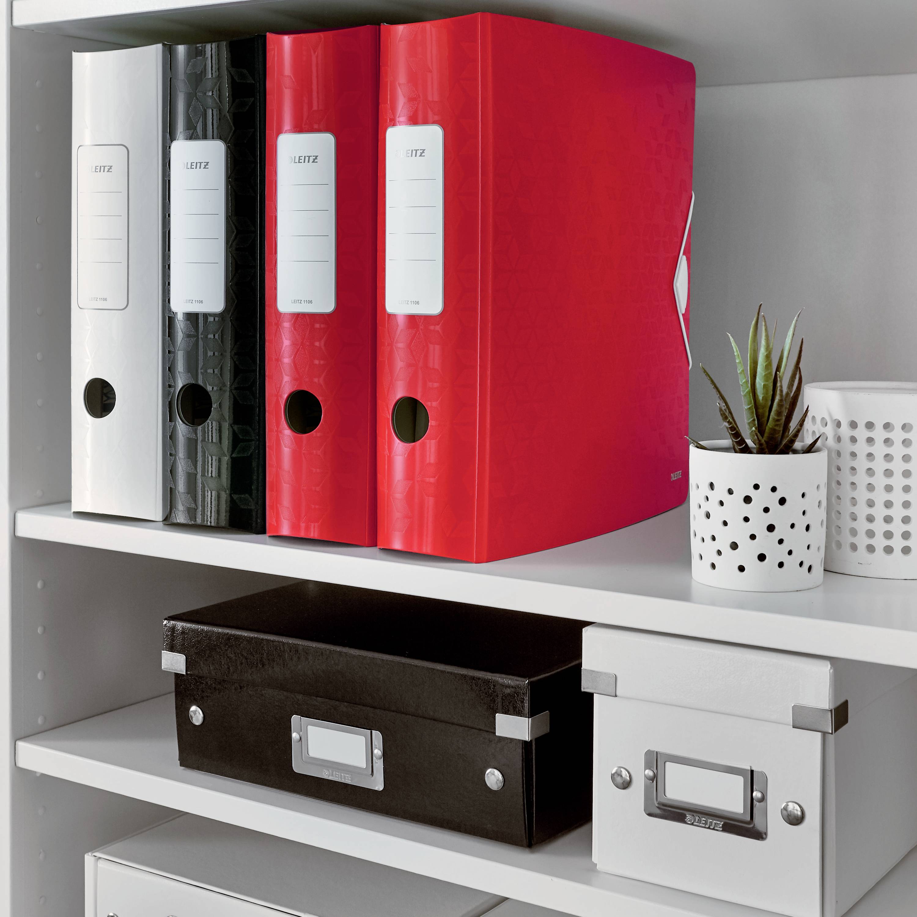 A shelf with three folders, including a standout red one, next to a small pot with a green plant. Below that, two boxes.