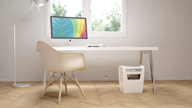 Modern desk with a white chair, computer with a colourful screen protector, positioned in front of a window. A small paper shredder is also present in the room.