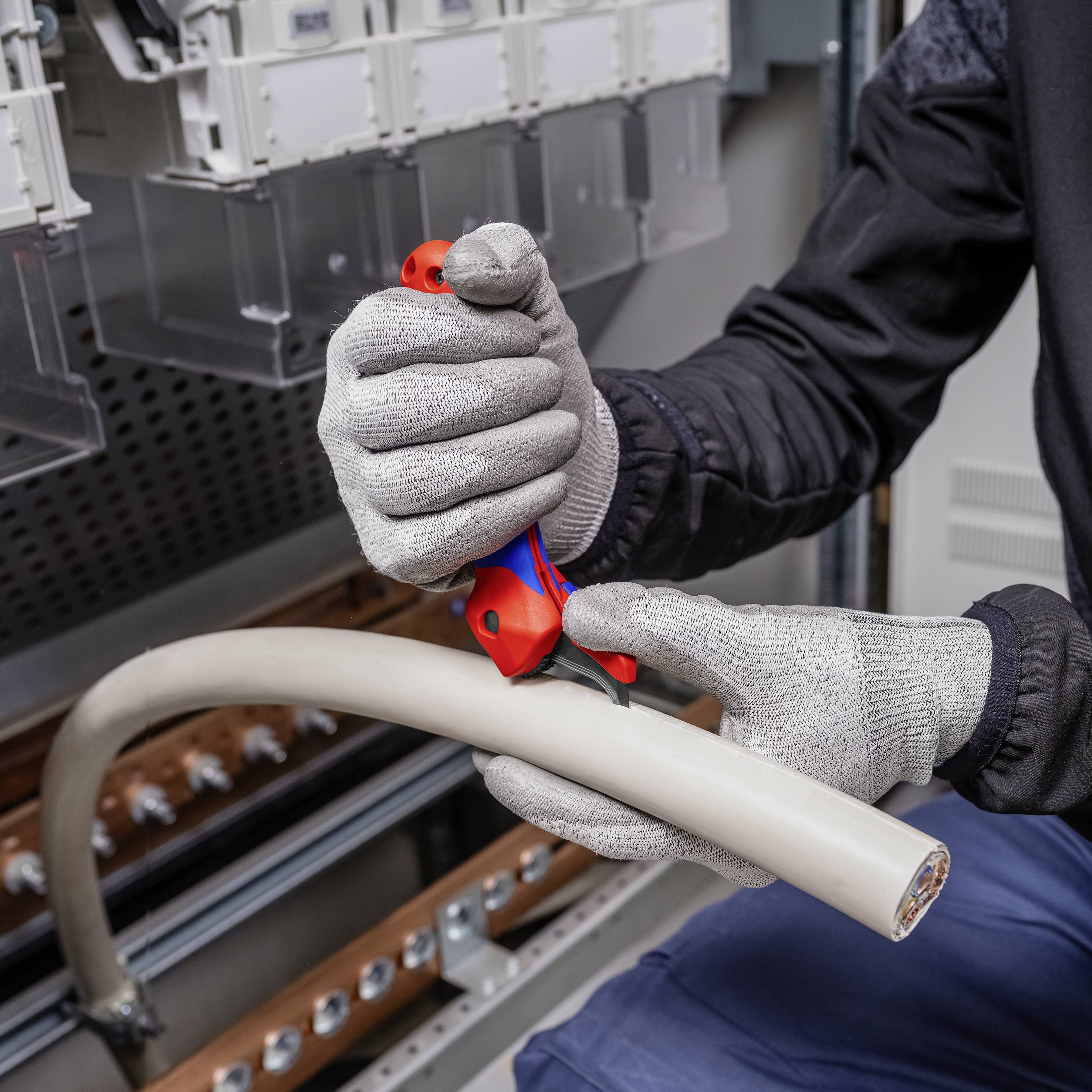 A person is cutting a thick cable with a tool in an industrial environment. They are wearing protective gloves.