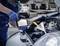 A mechanic wearing blue gloves is pouring oil through a funnel into the open engine of a car in a workshop.