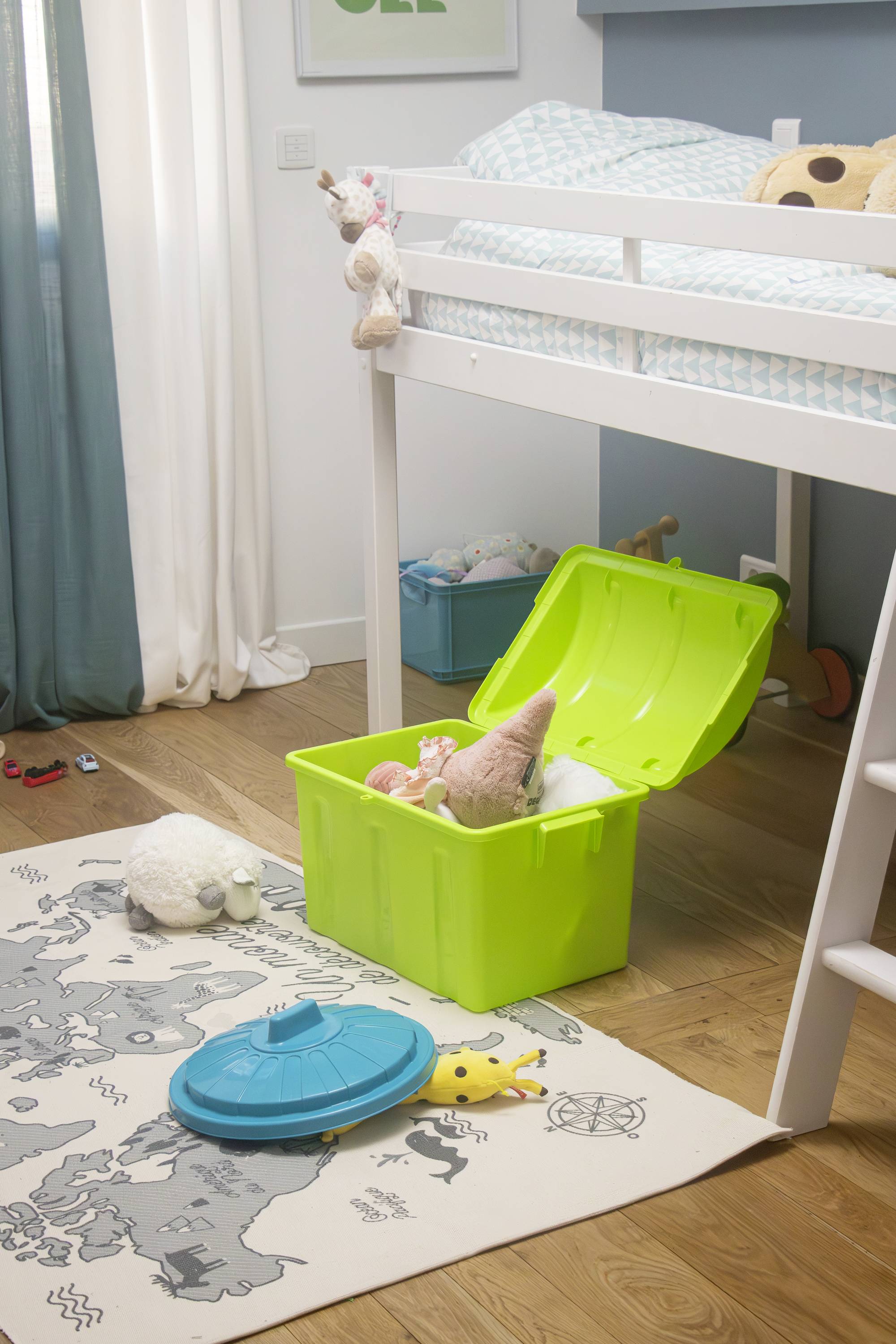 A children's bedroom with a bunk bed, beneath which an open green toy chest is located. Toys are scattered on the carpet.
