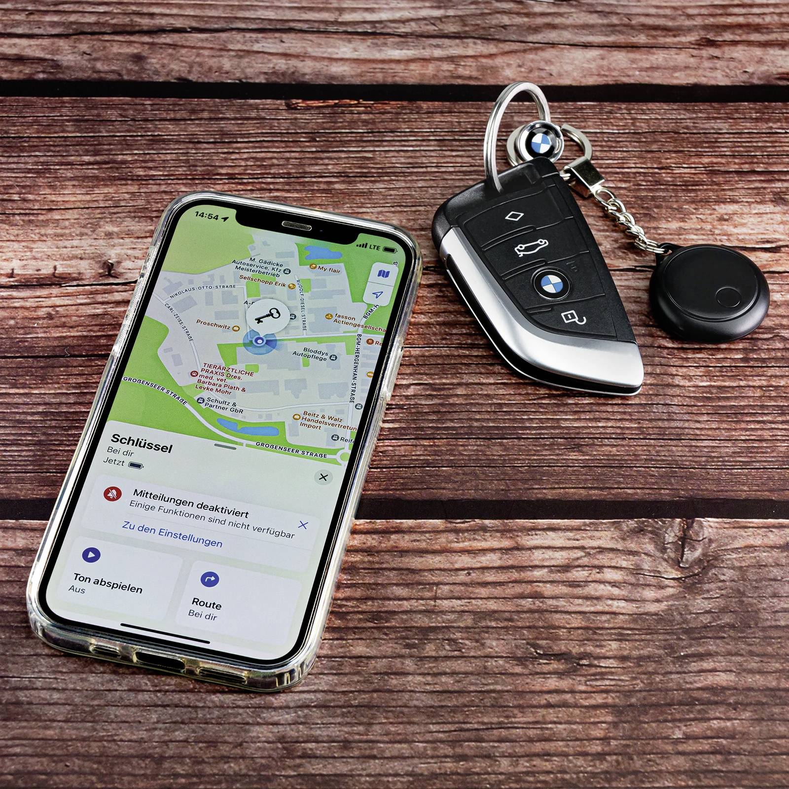 A smartphone with an open navigation app and car keys are lying on a wooden table. The app displays a route plan to the destination.