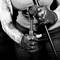 A person with tattooed arms and gloves is holding a bar. The focus is on the hands and the bar. Black and white format.