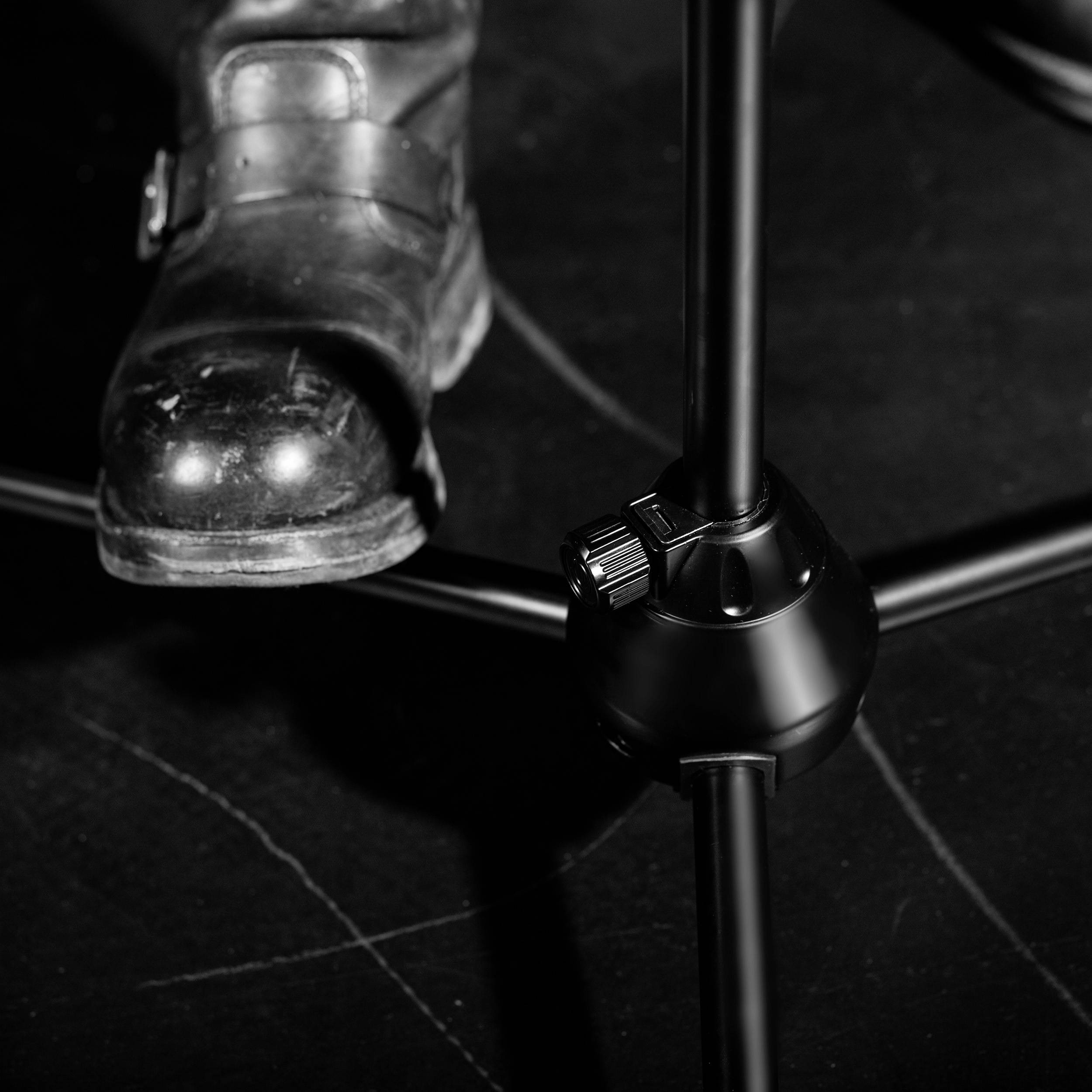 A boot steps onto a stage beside a microphone stand, depicting a close-up of concert preparation.