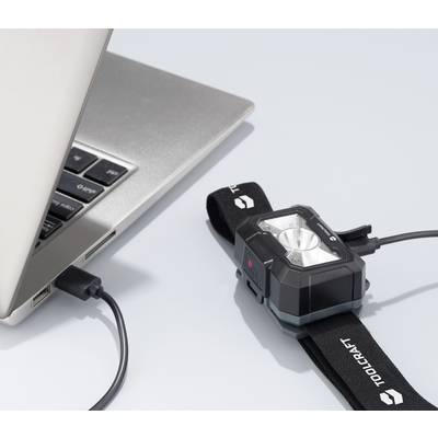 A camera is connected to a laptop via a USB cable, charging or synchronising data. The camera is branded 'TOOLCRAFT'.