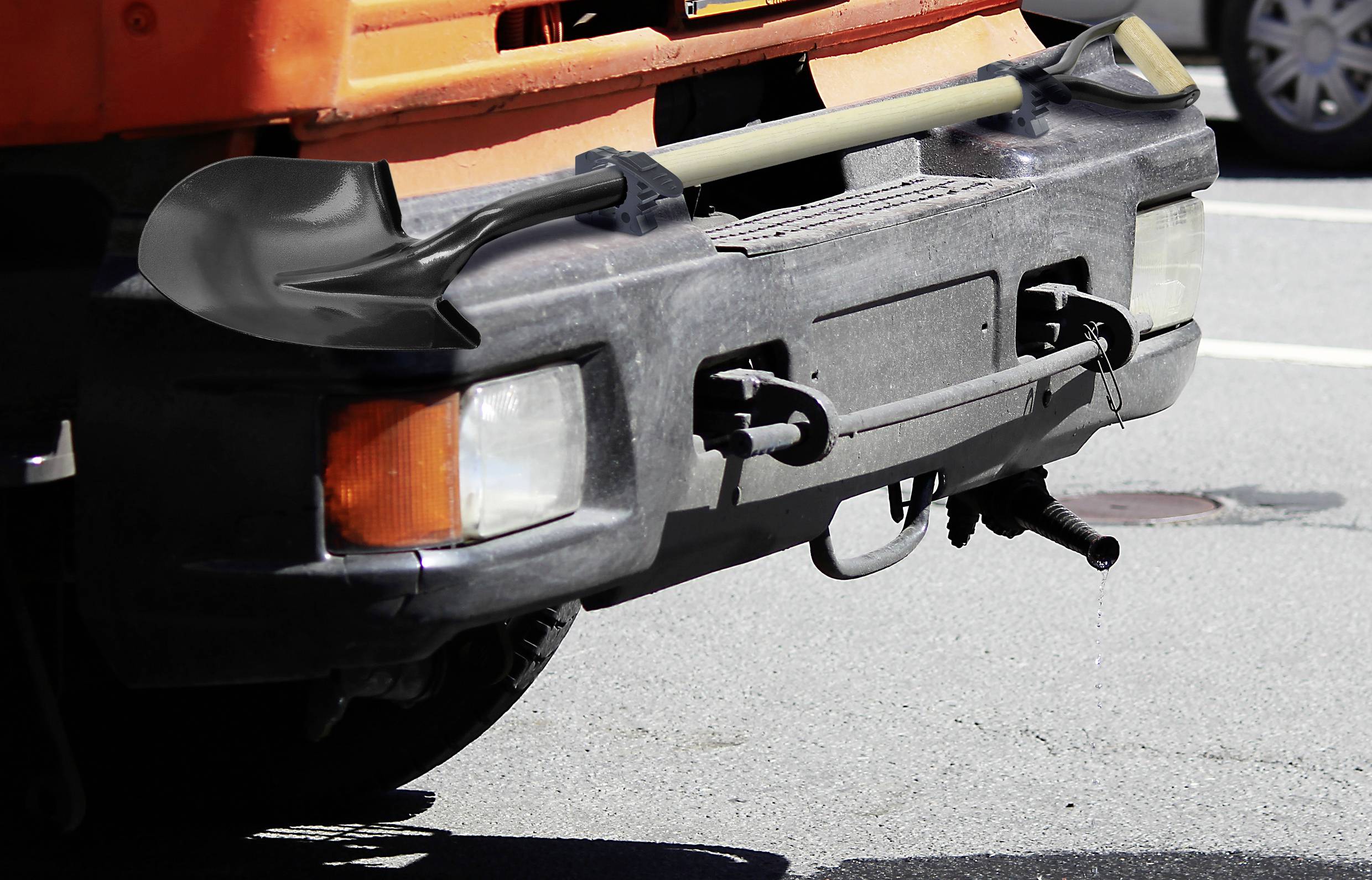 A lorry with a shovel laid horizontally across the front bumper is parked on an asphalt surface.
