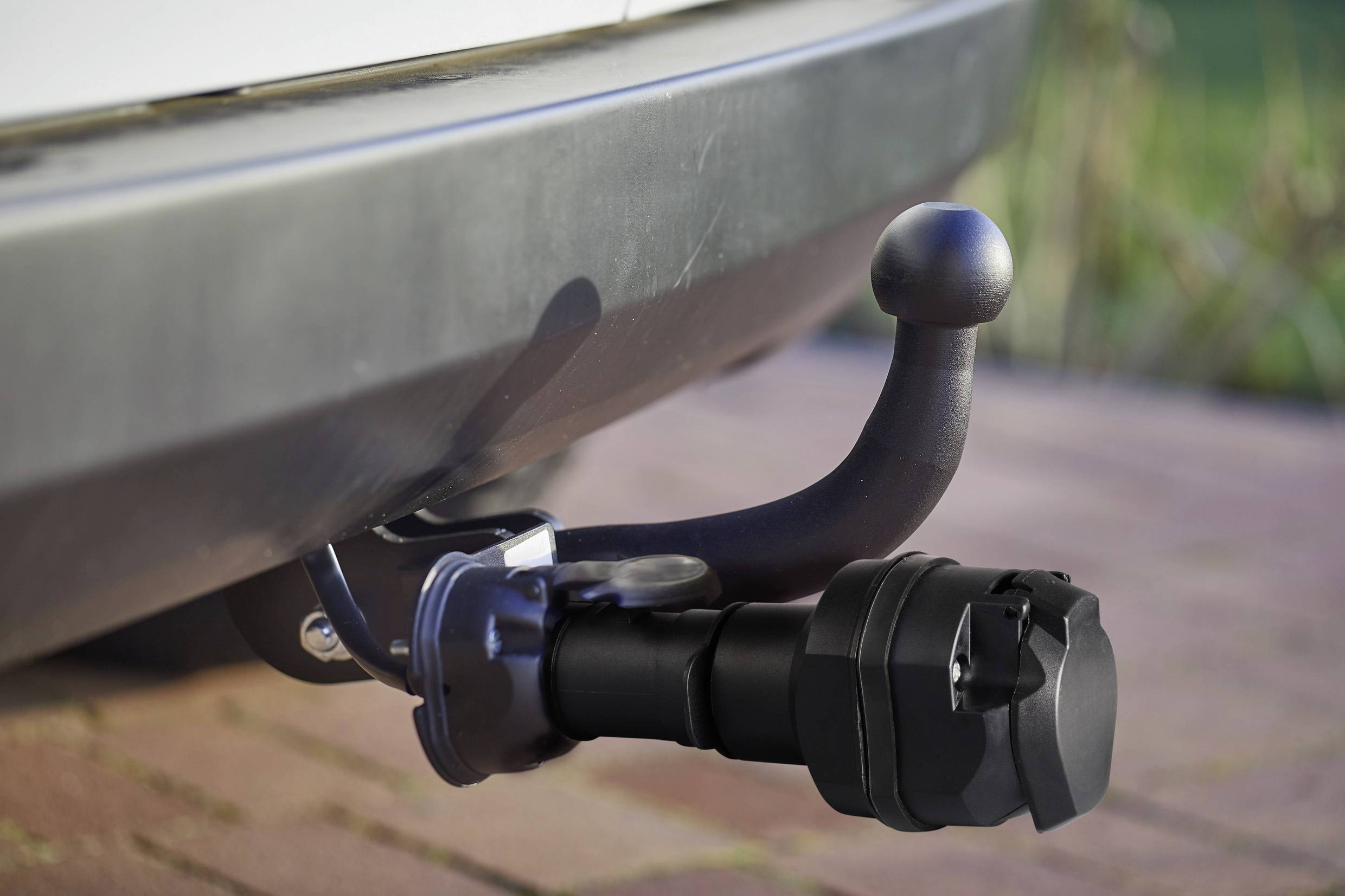 A tow bar on a car, pointing downwards. It is black and made of metal, and is situated on the rear bumper.