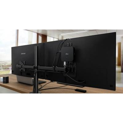 Two large monitors on a desk, rear view, connected to a small black box. Office environment in the background.