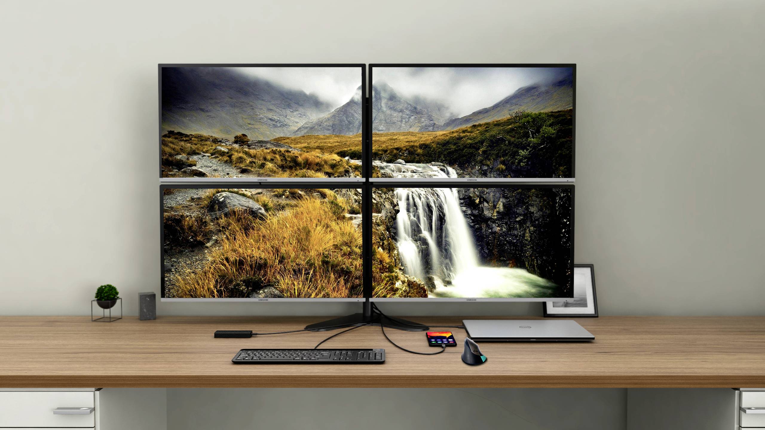 Four connected monitors display a landscape image featuring a waterfall and mountains. A keyboard and mouse are positioned in front of them.