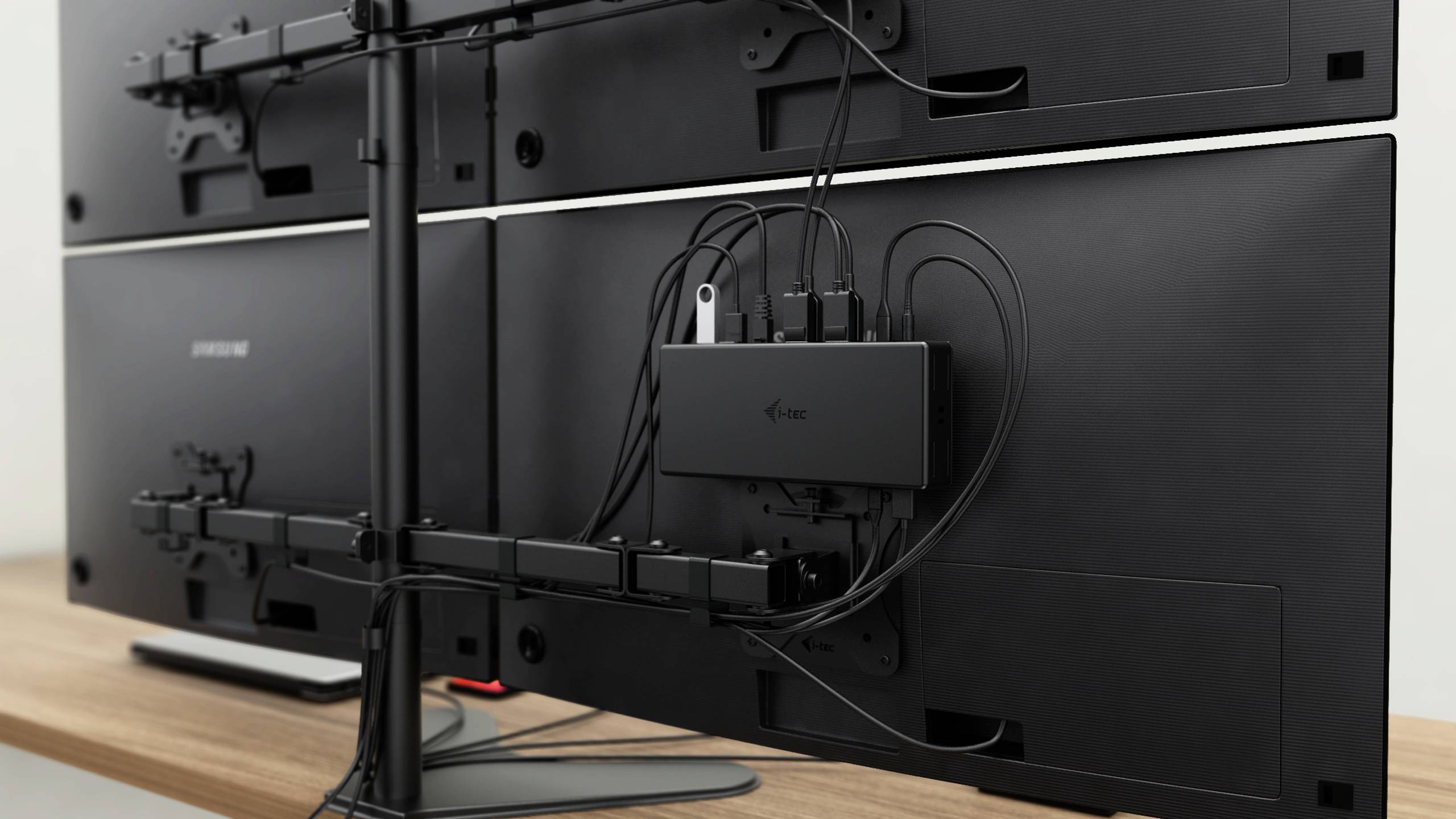 Four monitors are connected at the back with cables to a black box mounted on a black stand.