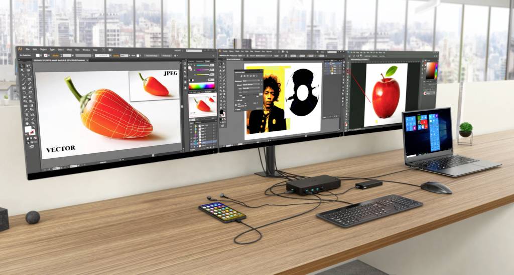 A desk with a laptop, several large monitors displaying graphic design software, and a keyboard.