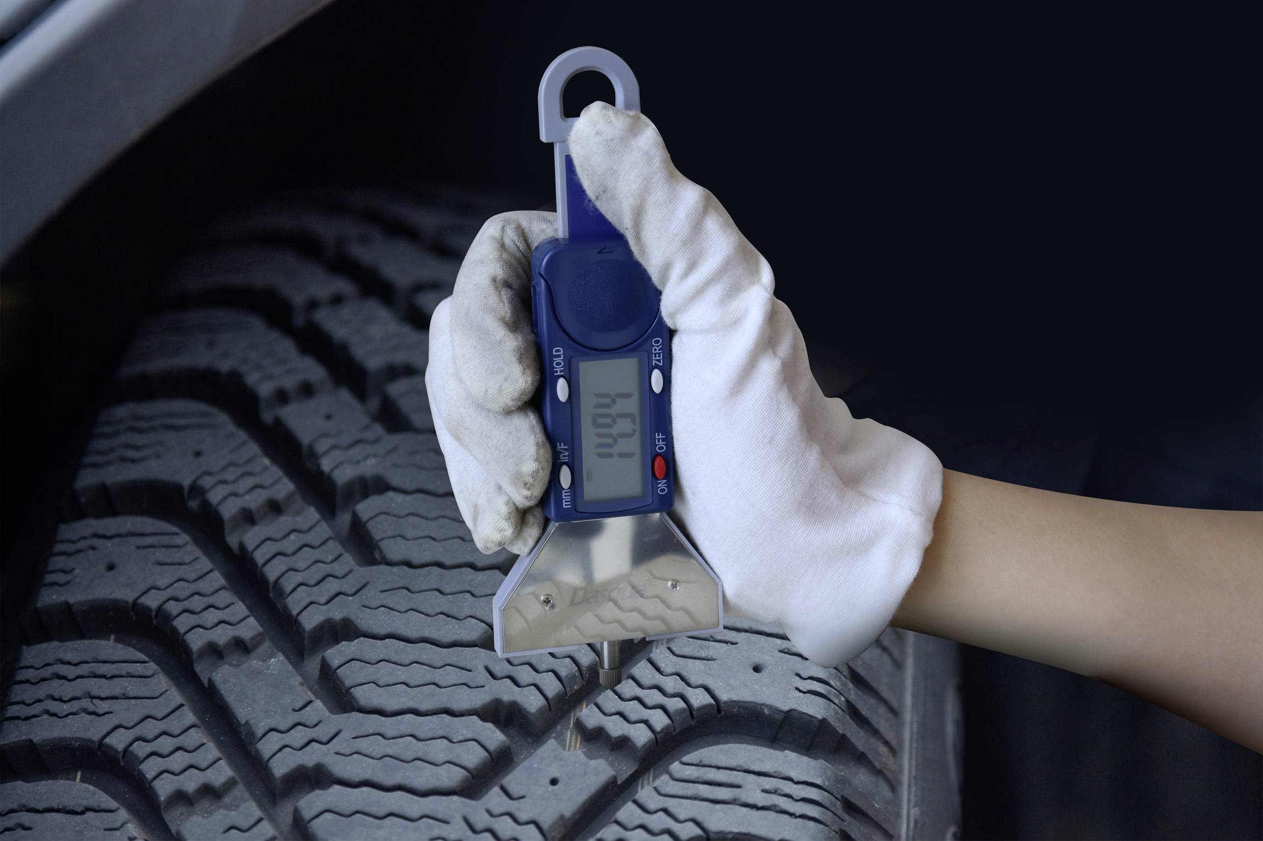 A person is measuring the tread depth of a car tyre using a digital measuring device.