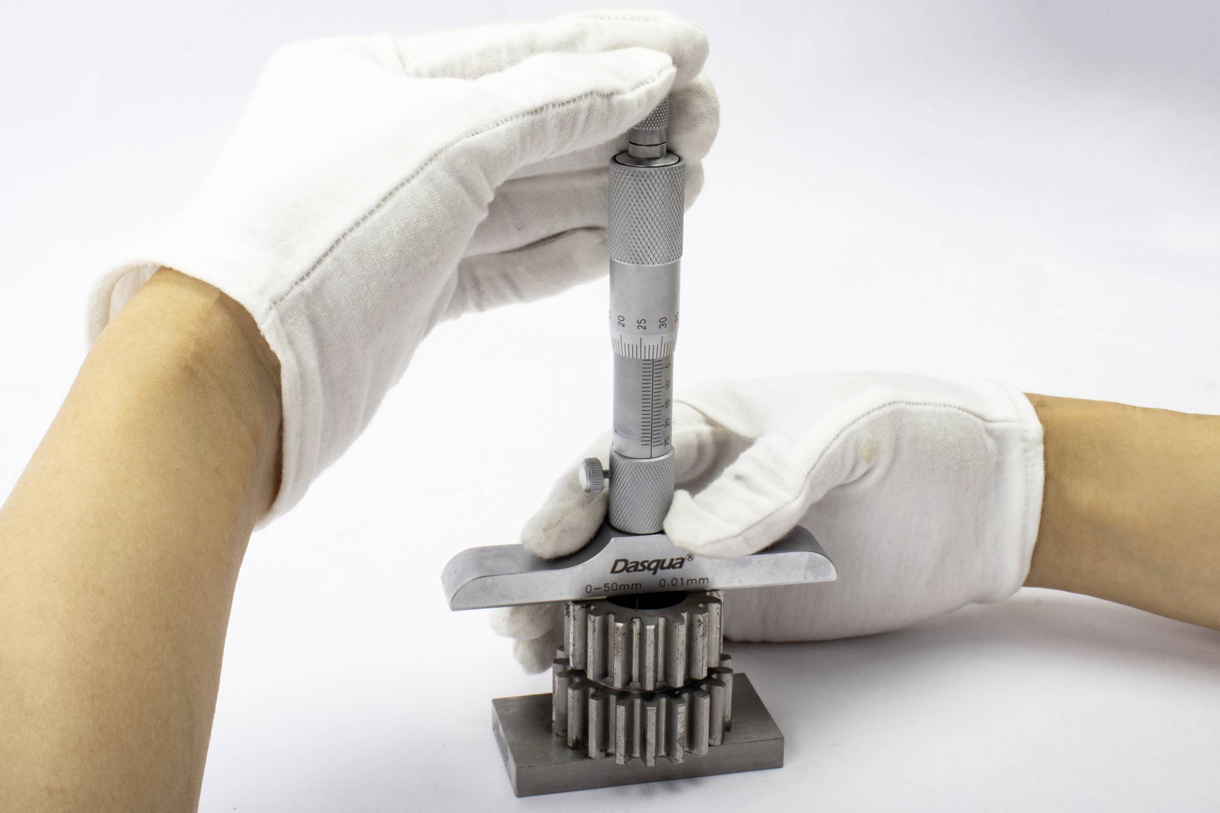 A person wearing white gloves is measuring the thickness of a metal object with a measuring device. Focus on precision and control.