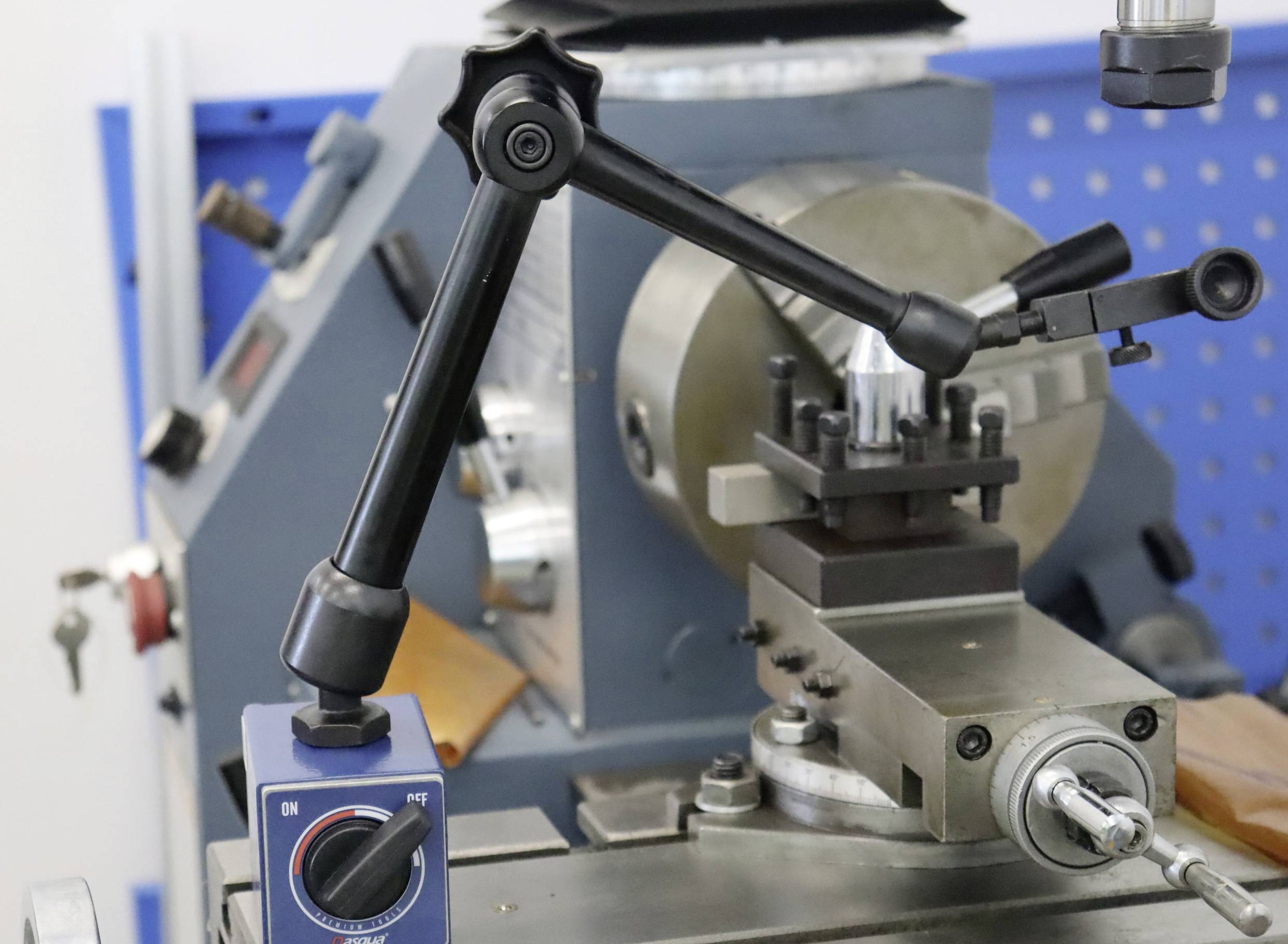 Lathe with precision adjustment and tooling, ready for metal machining. Blue perforated metal sheet in the background.