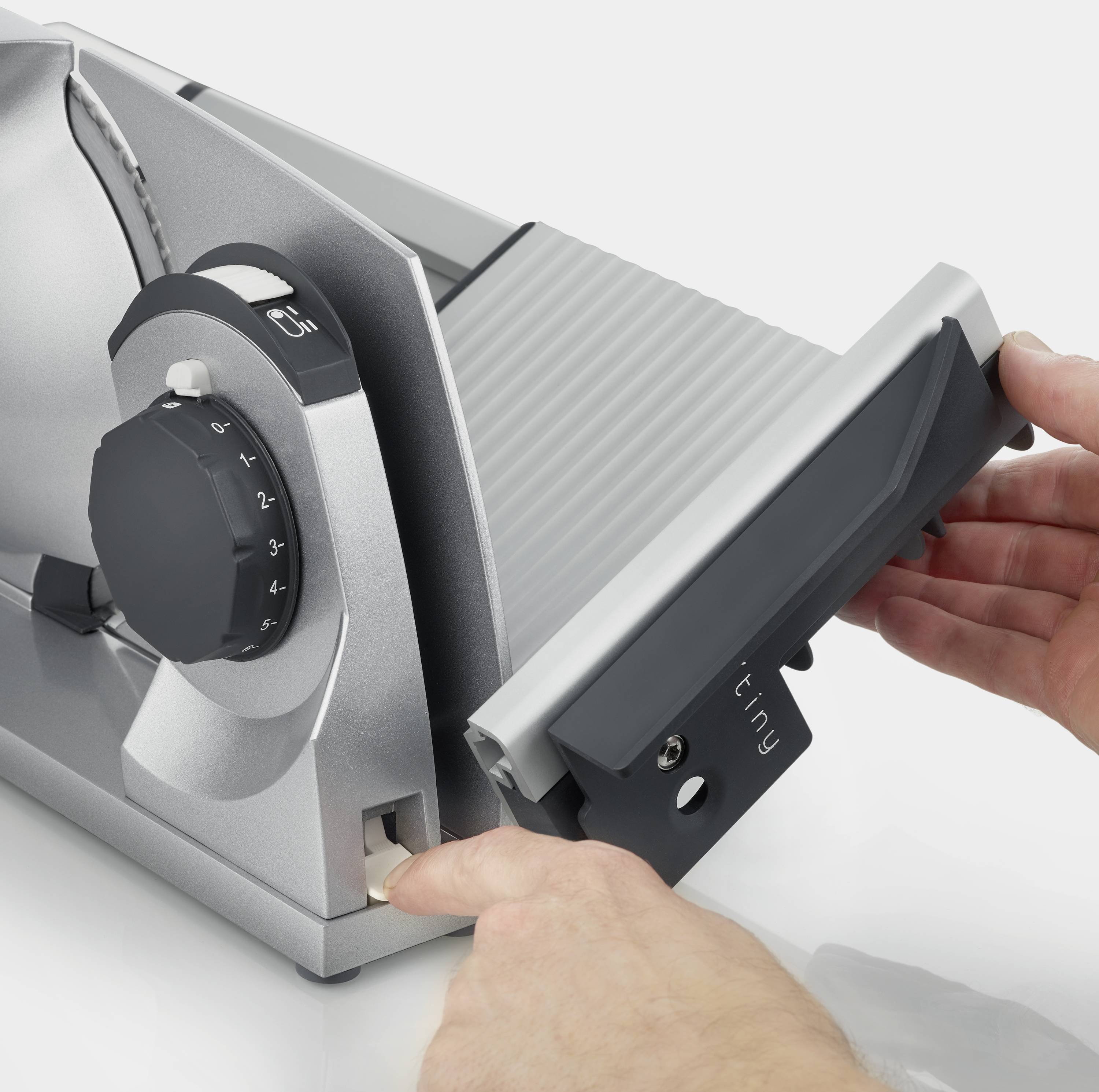 A person is operating an electric food slicer by adjusting the thickness and placing a piece of food on the cutting board.