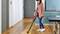 A woman is cleaning crumbs from the wooden floor with a cordless vacuum cleaner in a modern kitchen.