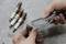 A person is measuring the electrode gap of a spark plug with a feeler gauge. Several used spark plugs are lying in the background.