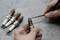 A person is checking spark plugs with a screwdriver. Four additional spark plugs are lying on a workshop bench.