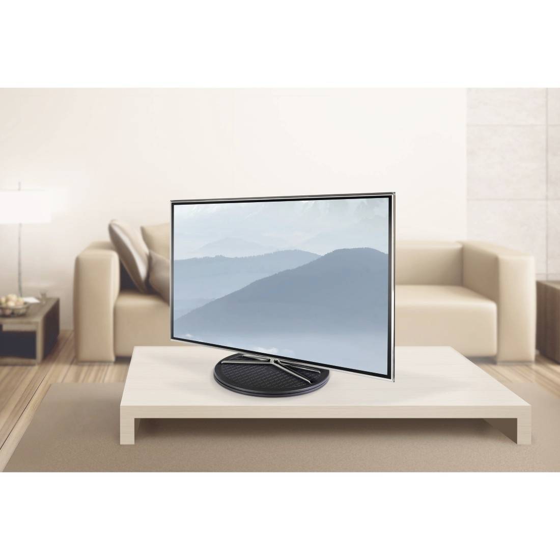 Flat-screen television on a low table in front of a sofa. The screen displays a landscape image with mountains in the background.