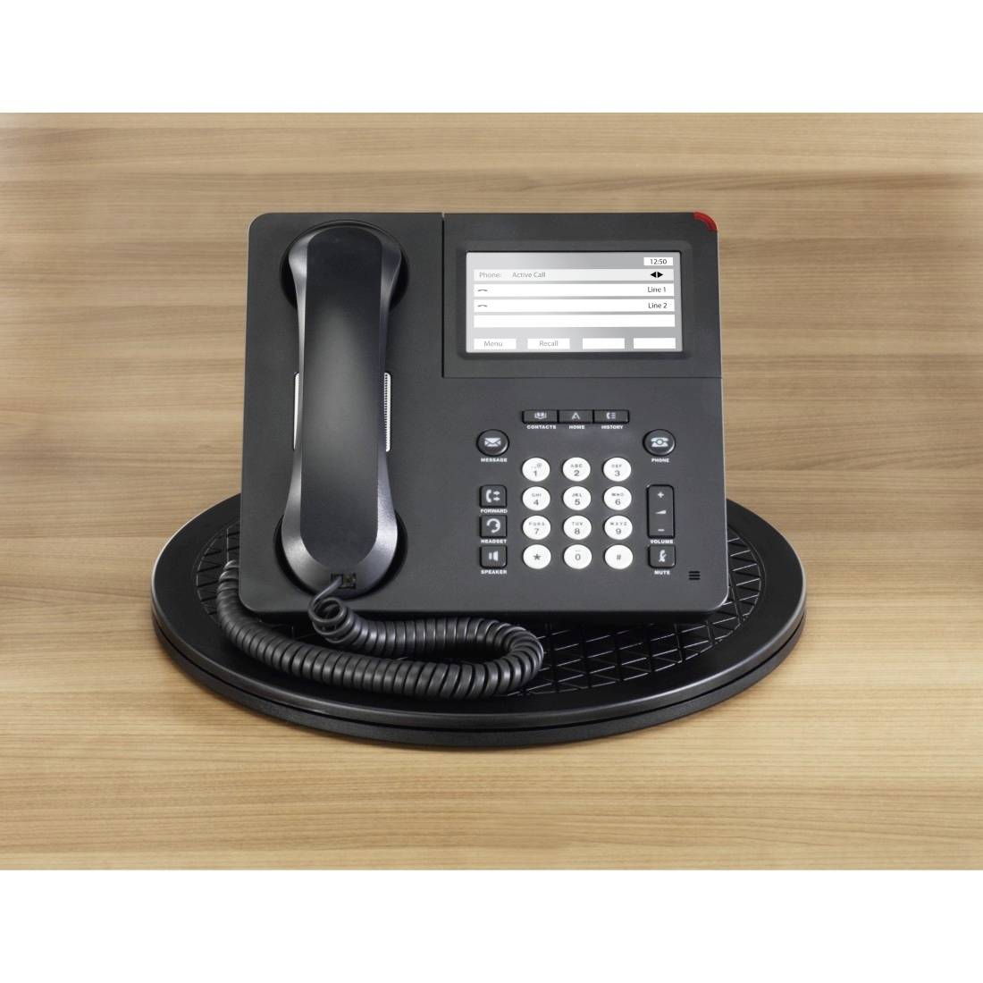 A black desk telephone with a display and number keys sits on a round coaster on a wooden table.
