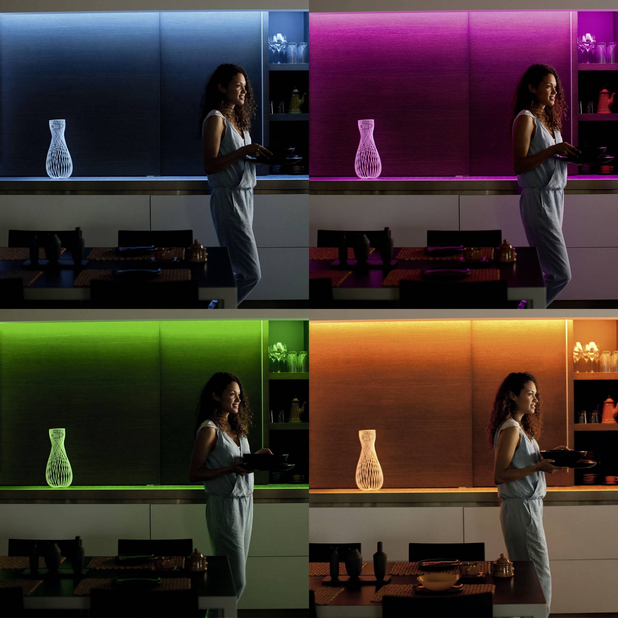 A woman is standing in front of a table in a room with changing coloured lighting (blue, pink, green, orange). She is holding a tray.