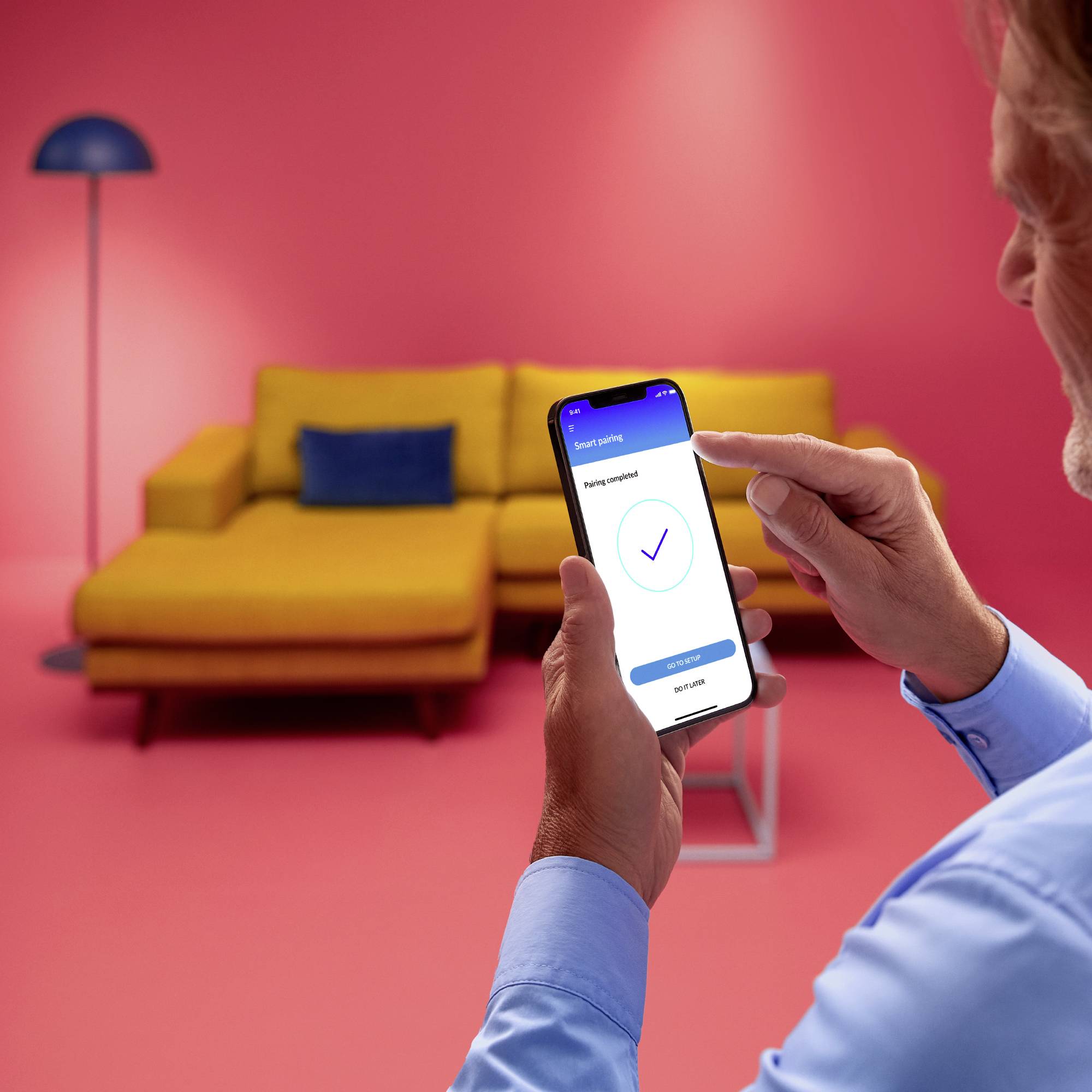 A hand holds a smartphone displaying an app indicating a successful payment. In the background, a yellow sofa.