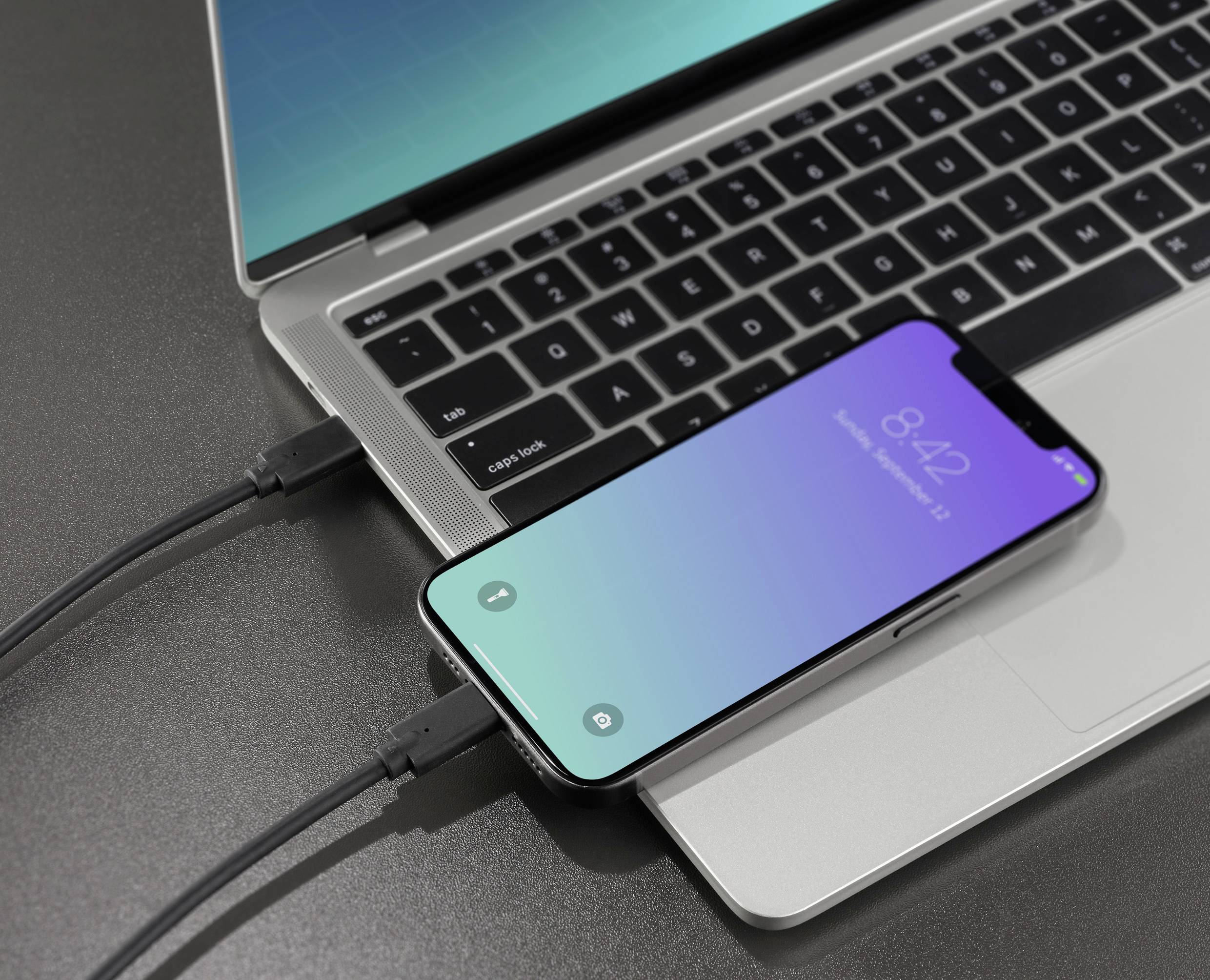 A smartphone is connected to a laptop via a USB cable, with both devices showing charging activity.