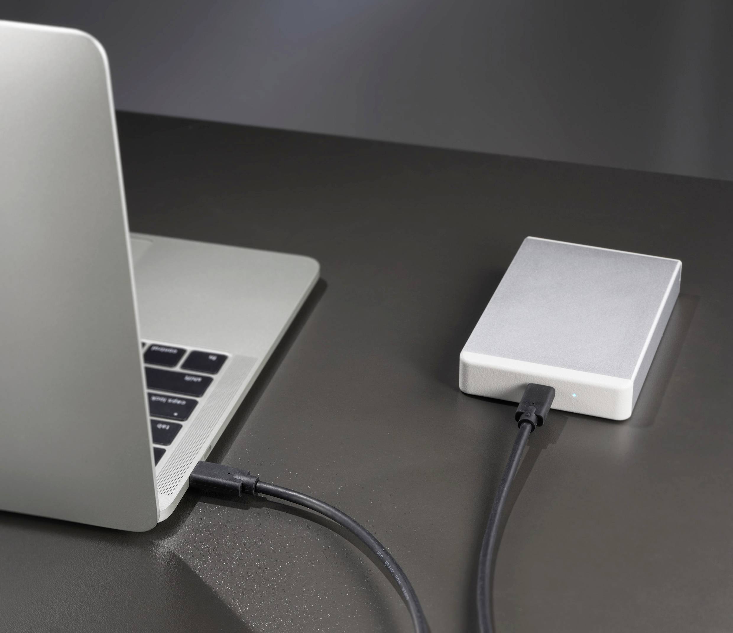 A laptop is connected via a cable to an external hard drive, which is sitting on a table.