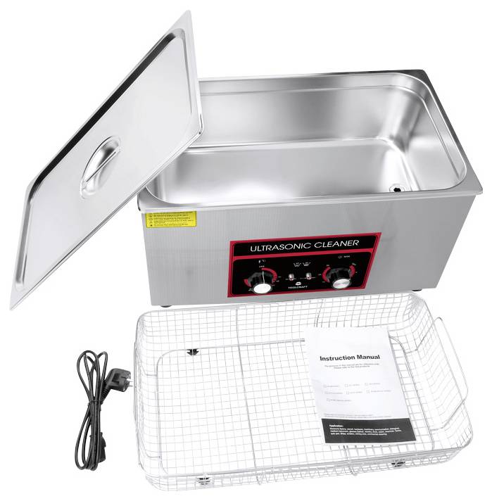 An ultrasonic cleaner with an open lid, showing control buttons and a removable wire basket. A power cable and instruction manual are also visible.