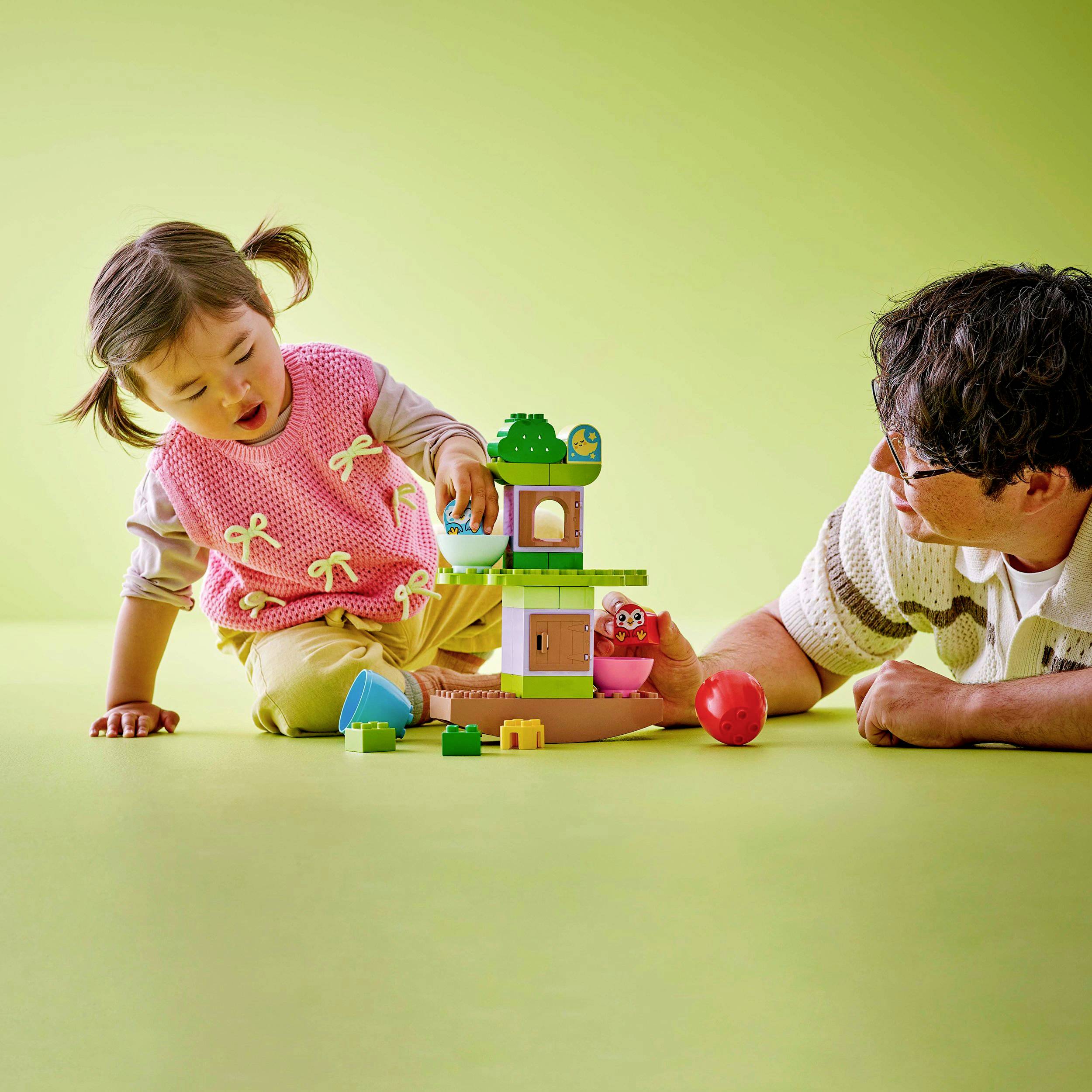 A child and an adult are playing together and building a tower with colourful building blocks, both smiling.
